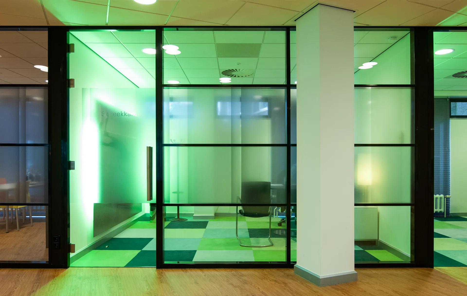 Ingang met glazen deur naar een moderne kantoorruimte met groene verlichting, wat een professionele sfeer ademt.