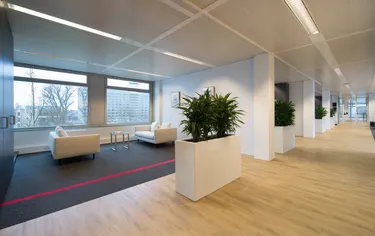 Een moderne kantoorruimte met een strak en minimalistisch ontwerp, voorzien van een groot raam, witte meubels en enkele planten.