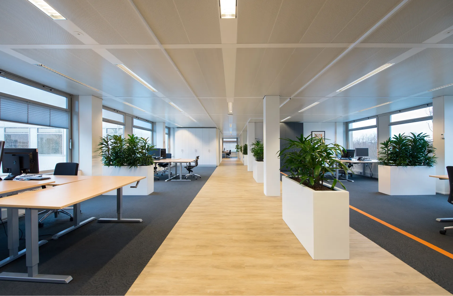 Een moderne kantoorruimte met een lange, open indeling, een centrale gang met witte muren, omringd door rijen bureaus en stoelen.