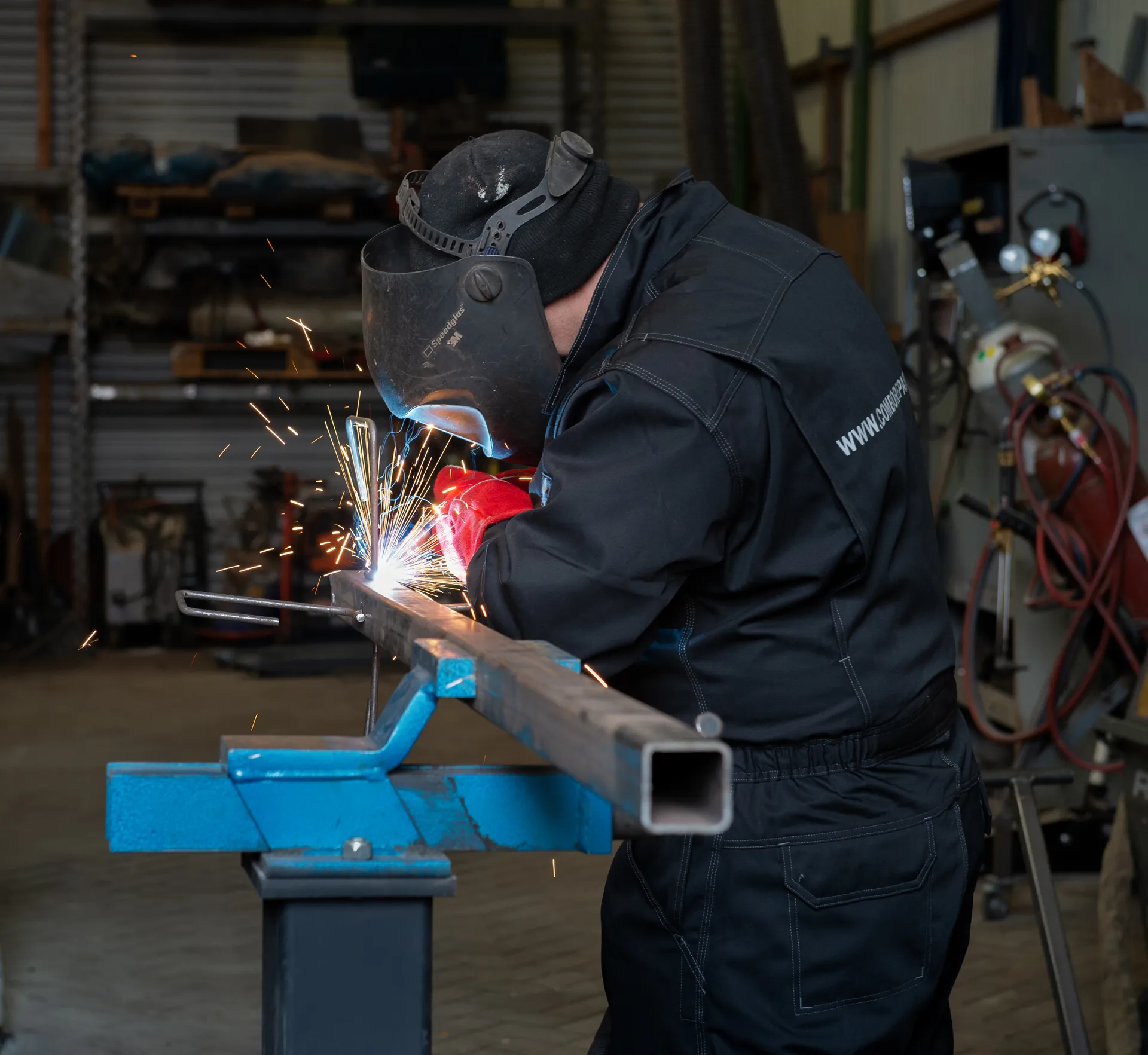 Een persoon in beschermende kleding last metaal in een industriële werkplaats, waarbij veel vonken vrijkomen.