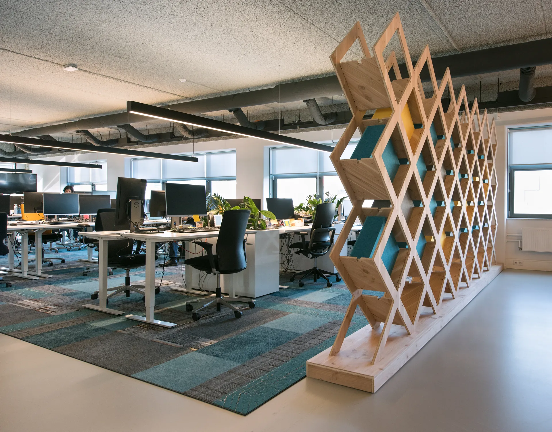 Open-concept kantoorverdieping met witte muren, blauw/grijze vloerbedekking en scheidende halfhoge kastenwanden.