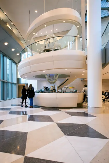 Een modern kantoor atrium met een grote witte wenteltrap, een geblokte zwart/wit-vloer en een balie met een glazen vitrine.